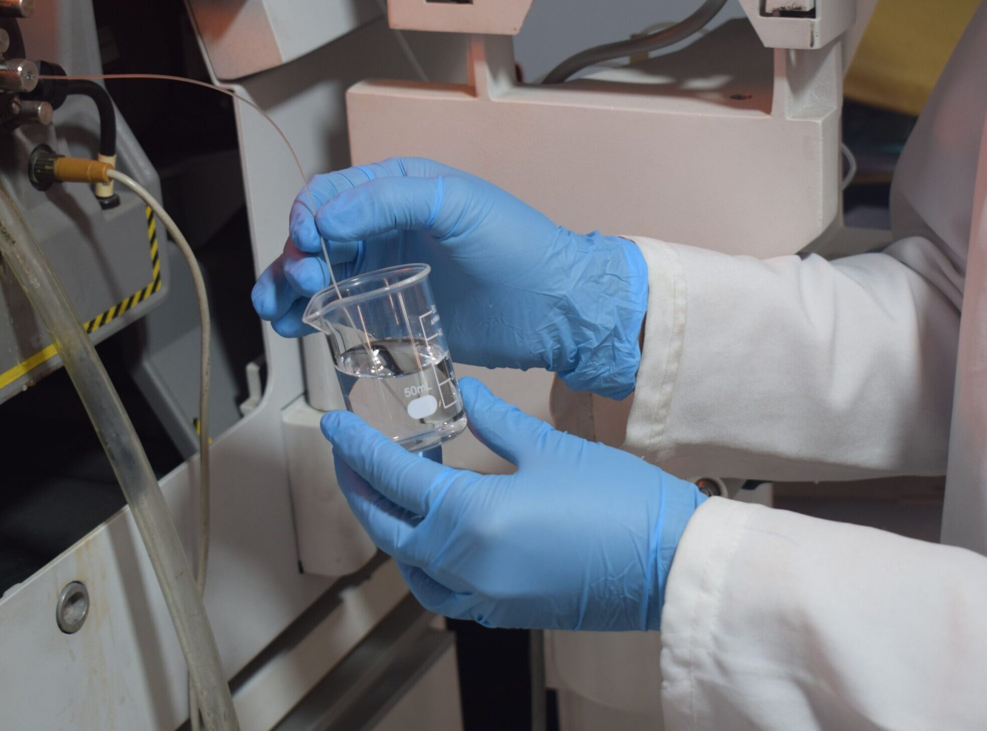Gloved hands test liquids in a beaker in a lab.