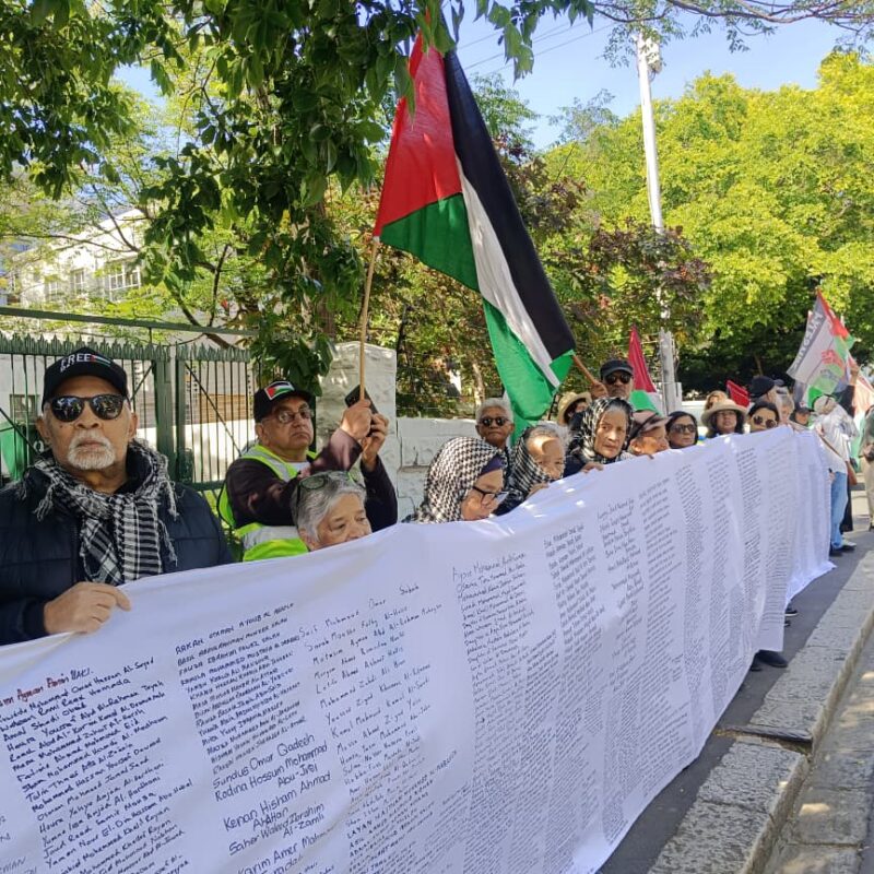 pro-palestine protestors stand in Cape Town. they hold a long banner with thousands of name of children killed in Gaza.
