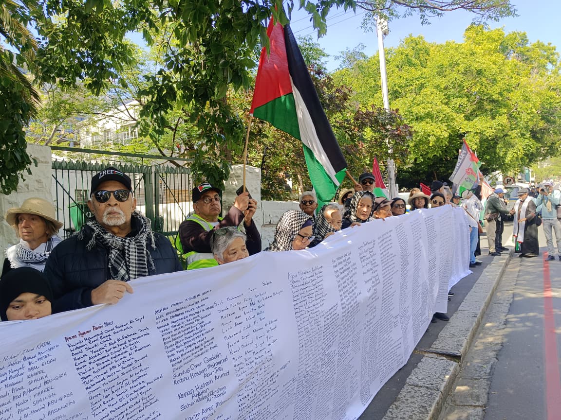 pro-palestine protestors stand in Cape Town. they hold a long banner with thousands of name of children killed in Gaza.